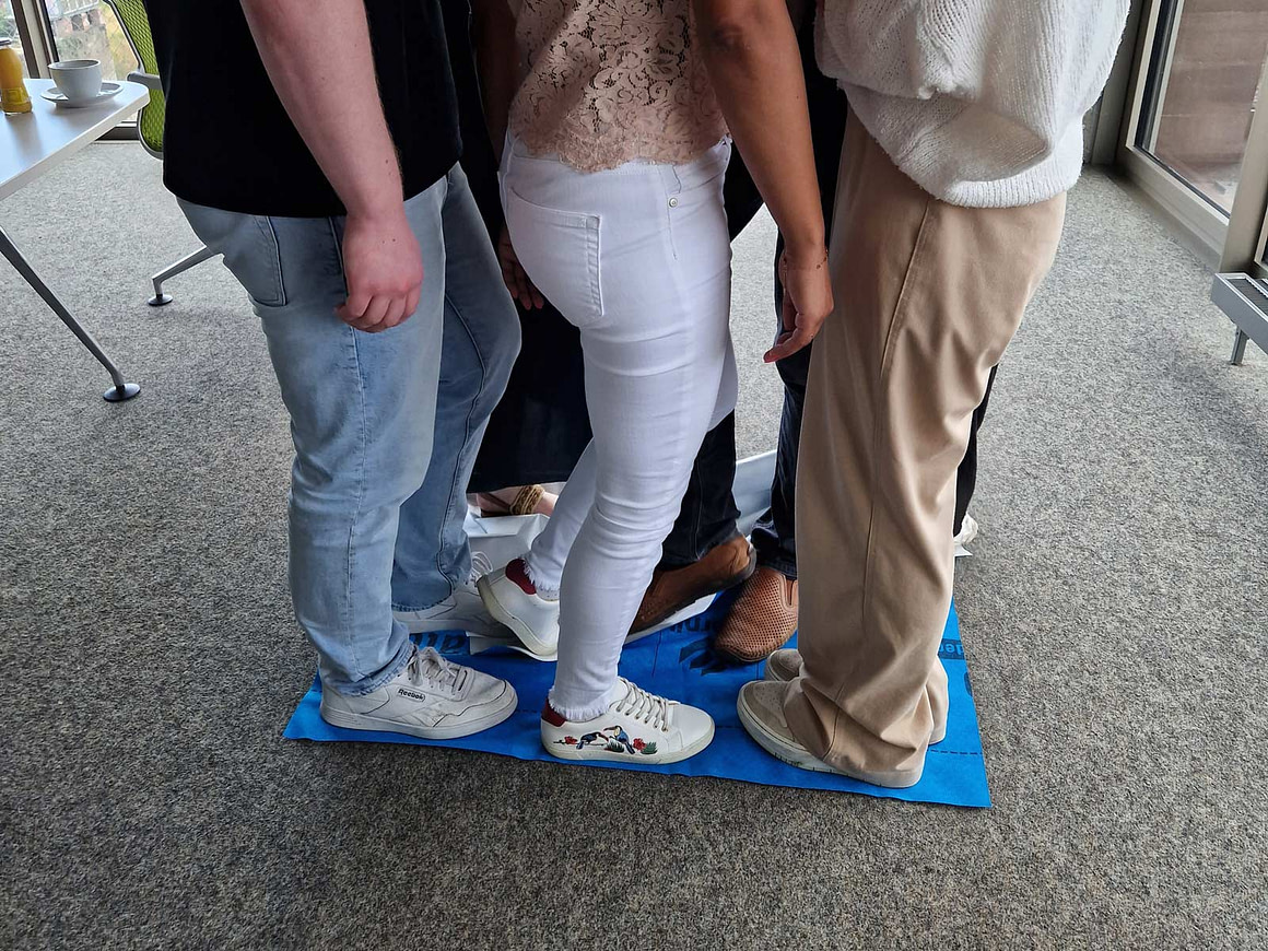 Zusammenhalt und Nähe im Team stärken Teamentwicklungs-Übung, Gruppe steht dicht zusammen auf Matte