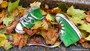 Kleine grüne Kinderschuhe im Herbstlaub – Symbolbild für negative Glaubenssätze aus der Kindheit, die wir längst hätten ablegen können