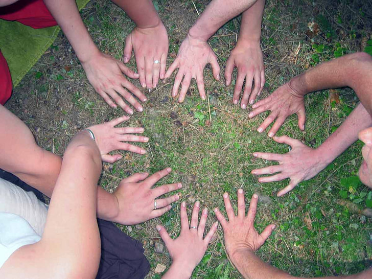 Viele Hände von Gruppenteilnehmern bilden auf dem Boden einen Kreis als Symbol für Gemeinschaft, Kooperation und erfolgreiches Teambuilding.