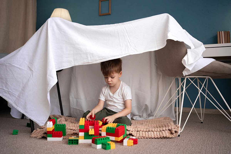 Hochsensible Kinder brauchen Rückzugsorte Hochsensibles Kind baut sich Rückzugsort: Kleines Kind spielt in selbstgebauter Höhle aus Decken. Zeigt Bedeutung von sicheren Rückzugsräumen für überreizte hochsensible Kinder.