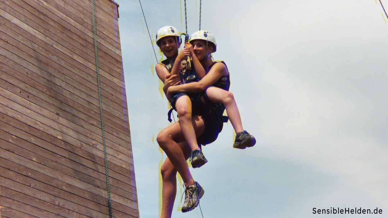 glückliches Herabkommen Zwei Geschwister hängen strahlend am Seil nach ihrer gemeinsamen Überwindung im Hochseilgarten Worms